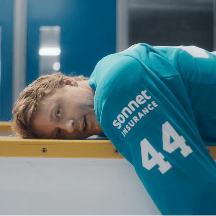 Morgan Rielly of the Toronto Maple Leafs wearing a teal Sonnet Insurance jersey with number 44, lying on the boards inside a hockey arena.